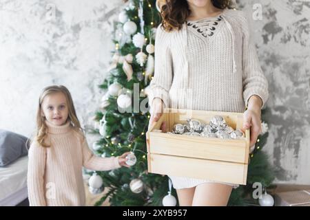 Frau mit ihrer Tochter, die eine Box mit viel Weihnachten silber Dekorationen in der Nähe der Weihnachtsbaum. Weihnachten Konzept Stockfoto