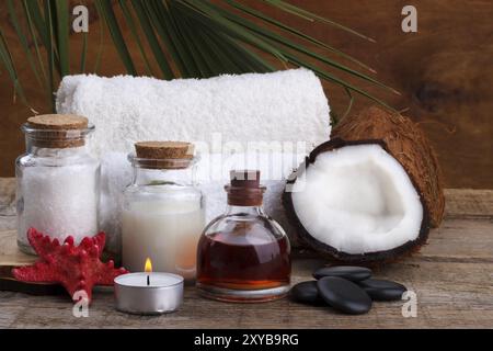 Spa-Setting und Gesundheitsartikel, Kokos, Körperöl, Badesalz, Milch, Massagesteine und Handtücher, auf Holzbrett Stockfoto