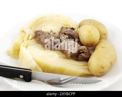 Gekochtes Fleisch und Kohl, mit Kartoffeln, Messer und Gabel, weiße Platte zu weißem Hintergrund Stockfoto