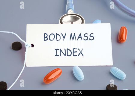 Medizin und Body Mass Index Konzept. Kopierbereich. Konzeptwort Body Mass Index auf einer weißen Karte auf grauem Hintergrund. Konzeptfoto Stockfoto