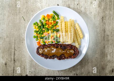 Ein Teller mit einem Stück Lendenfleisch, Gemüsemischung und Pommes frites Stockfoto