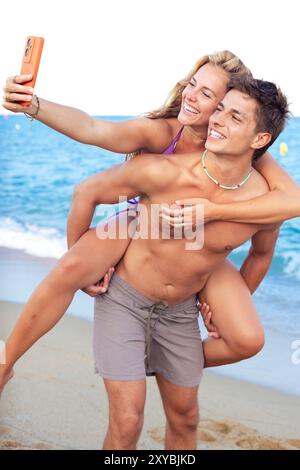 Glücklicher Mann, der seine Freundin auf dem Rücken trägt und Spaß am Strand hat Stockfoto
