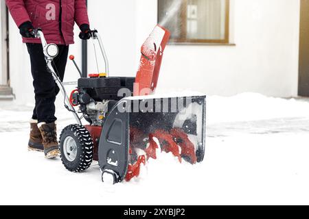 Nahaufnahme der roten Schneefräse in Aktion. Erfahrener Mann vor dem Haus mit Schneefräse, um Schnee auf dem Hof zu entfernen. Schneefräse rein Stockfoto