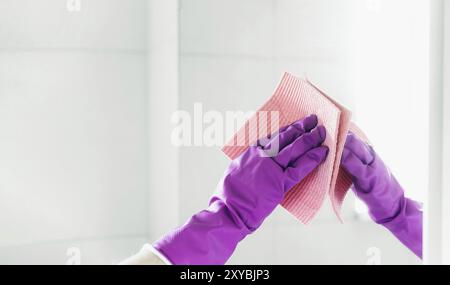 Verkürzter Blick auf die Haushälterin Hand in violetten Gummihandschuhen Polierspiegel mit pinkfarbenem Lappen Reiniger beim Reinigen des Badezimmers zu Hause. Haushälterin Stockfoto