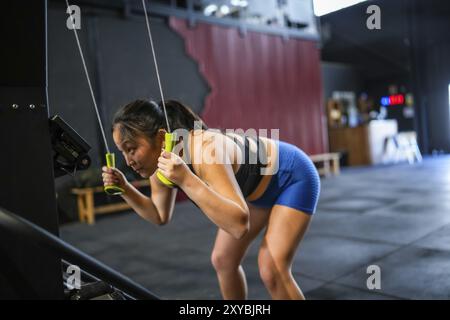 Seitenansicht einer Chinesin, die in einem Cross-Training-Fitnessstudio Gewichte mit Latmaschine zieht Stockfoto