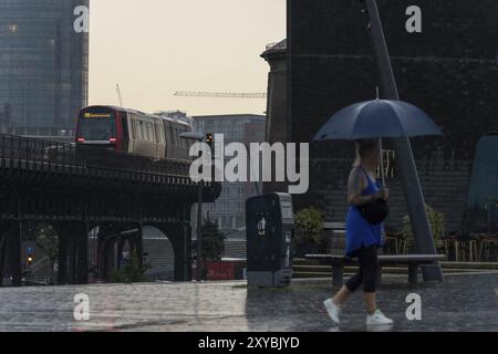 Symbolisches Bildwetter, starker Regen im Sommer, Gewitter, Sturm, Tourist mit Schirm unterwegs im Regen neben der U-Bahn-Linie U3 bei t Stockfoto
