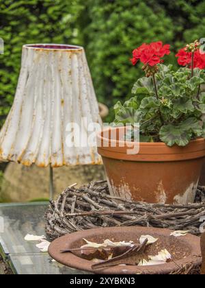 Ein Blumentopf mit roten Blüten steht neben einer weißen, rustikalen Lampe vor grünem Hintergrund im Garten, borken, münsterland Stockfoto