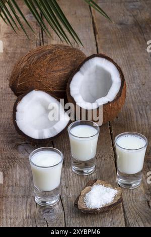 Kokosmilch im Glas mit Kokosnussschalen auf altem hölzernem Hintergrund, selektiver Fokus Stockfoto