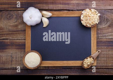 Knoblauchzehen, Knolle, Flocken und Pulver auf altem hölzernem Hintergrund mit schwarzer Tafel für Text Stockfoto