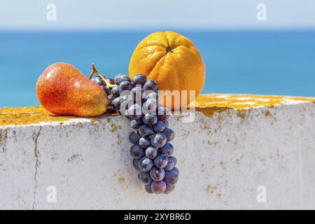 Trauben orange und Birne liegen auf Wand mit Himmel und Meer Stockfoto