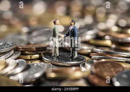 Kleine Figuren von zwei Männern, die auf einem Stapel Münzen die Hand schütteln Stockfoto