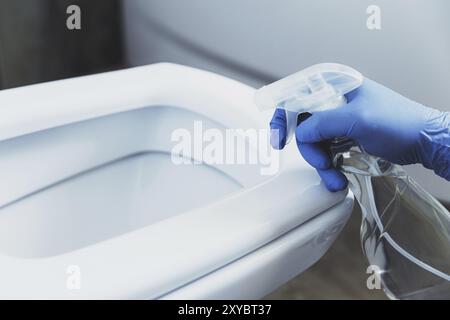 Nahaufnahme einer Frau mit Handschuhen aus blauem Gummi. Hausfrau reinigt Toilettenschüssel, Sitz mit Waschmittel im Bad oder auf der Toilette. Di Stockfoto