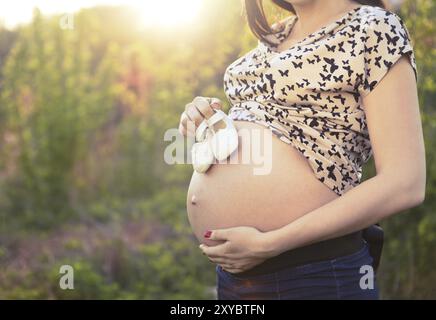 Nahaufnahme von unkenntlich schwangere Frau mit Baby Schuhe wenig auf ihrem Bauch bei Sonnenaufgang Hintergrund Stockfoto