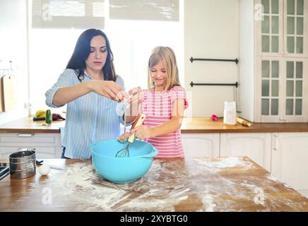 Glückliche junge Mutter und ihre Tochter gießen Mehl durch Sieb für Teig bei Küche Stockfoto