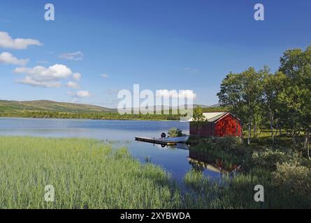 Rote Hütte an einem ruhigen Seeufer mit grasbewachsenen Ufern und Bäumen, blauem Himmel, Idylle, Glomma, Roeros, Troendelag, Norwegen, Europa Stockfoto