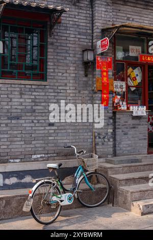 Ruhige Szene in einem traditionellen Pekinger Viertel mit Fahrrad, das an einer grauen Backsteinmauer geparkt ist. Stockfoto