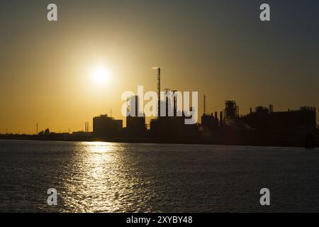 Eine Silhouette einer Petrochemie- oder Ölraffinerie auf dem Meer vor der untergehenden Sonne in Antwerpen, Belgien. Auswirkungen des Klimawandels und der globalen WPA Stockfoto