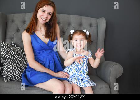 Junge Mutter und niedlichen kleinen Mädchen auf dem Sofa sitzt. Stockfoto