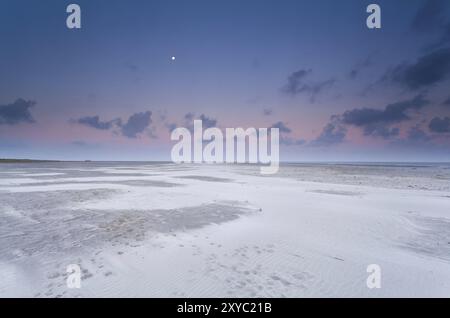 Vollmond- und Sonnenaufgangshimmel über dem Sandstrand auf der Nordsee Stockfoto