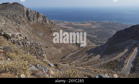 Panorama einer gewundenen Straße, die sich durch hügeliges Gelände bis zur Küste und zum blauen Meer erstreckt, kurvige Straße entlang der Kallikratis-Schlucht, Lefka Ori, Wh Stockfoto