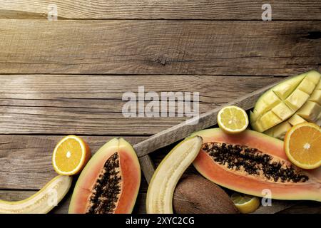 Frische tropische Früchte in einem Holzlieferkarton auf einem Holzhintergrund. Papaya, Orange, Banane, Kokosnuss, Mango und Zitrone Draufsicht flach mit Kopie sp Stockfoto