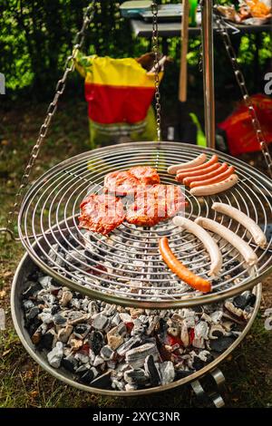 Steaks und Würstchen werden an einem Sommertag über dem Swinging Coal Grill gebraten Stockfoto