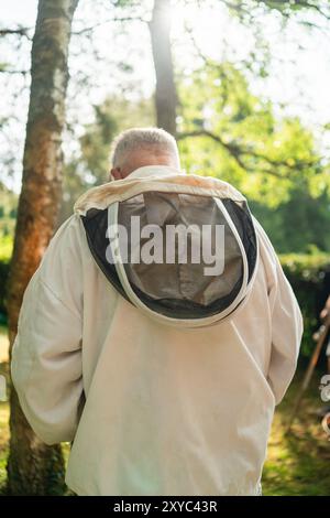 Imker bereitet sich auf die Imkerei der Bienen vor mit weißem Kapuzenanzug im hellen Sommersonnenlicht draußen in Green Nature Stockfoto