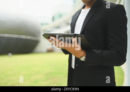 Zugeschnittene Aufnahme eines jungen Geschäftsmannes, der vor dem Bürogebäude steht und ein digitales Tablet verwendet Stockfoto