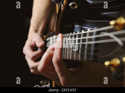 Nahaufnahme von Streichern und Gitarristen-Händen, die Gitarre über schwarzem, flachem DOF spielen, mit Fokus auf die Hände Stockfoto