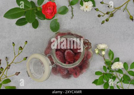 Gefrorene Himbeeren in einem Glas, dekoriert mit weißen und roten Rosen und Zweigen. Draufsicht. Stockfoto