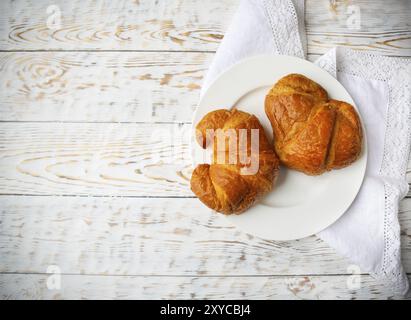 Zwei leckere Croissants auf dem Teller auf hölzernen Hintergrund. Ansicht von oben Stockfoto