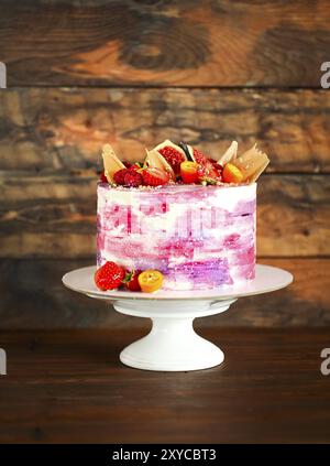 Schönes helles Kuchen auf ein Porzellan Kuchen mit Früchten dekoriert. Auf dem hölzernen Hintergrund Stockfoto