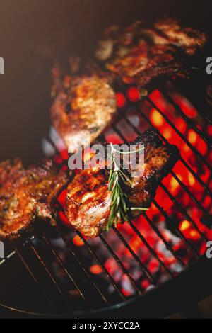 Von oben köstlichen, appetitlichen Fleischsteaks mit frischen Rosmaringrillen auf dem Regal über brennenden Kohlen Stockfoto