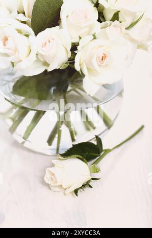 Von oben Komposition von weißen Rosen Bouquet in Glasvase mit Wasser und in der Nähe platzierte Blume auf weißem hölzernem Hintergrund Stockfoto