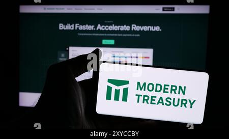 Person mit Smartphone und Logo des US-amerikanischen Geldbewegungsunternehmens Modern Treasury Corp. Vor der Website. Schwerpunkt auf dem Display des Telefons. Stockfoto