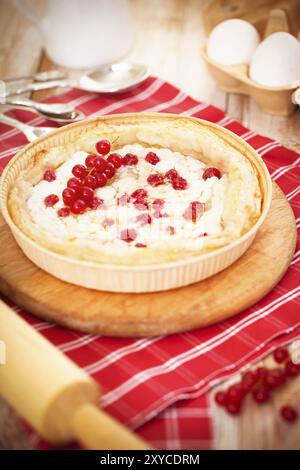 Von oben schmackhafter gebackener Käsekuchen mit kleinen roten Beeren auf Holzbrett auf dem Tisch Stockfoto