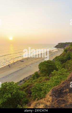 Hochwinkelblick auf Touristen am Strand und Meer während des Abendsonnenverkehrs, wenn die Sonne sich dem Horizont nähert in Varkala, Kerala, Indien. Vertikal Stockfoto