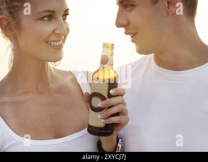 Paare am Strand feiern, trinken und Spaß im Sonnenuntergang haben, Flaschen in den Händen halten, während die Sonne durchscheint Stockfoto