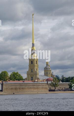 Die hohen Türme der St. Peter-und-Paul-Kathedrale mit ihren goldenen Türmen ragen vor einem bewölkten Himmel hervor, entlang eines Flusses, sankt petersburg, ostsee Stockfoto