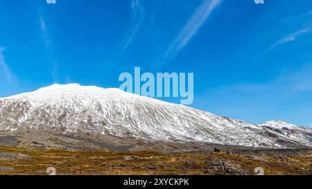 Ein schneebedeckter Berg steht hoch vor einem klaren, tiefblauen Himmel. Die Szenerie ist friedlich und ruhig, mit dem schneebedeckten Berg, der eine se bietet Stockfoto
