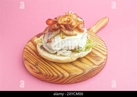 Hamburger, mit geschmolzenem Käse, Zwiebeln, Paprika, Speck, Ketchup, Senf, scharfer gemahlener Pfeffer, asturisches Rindfleisch, Spanien. Rosafarbener Hintergrund Stockfoto