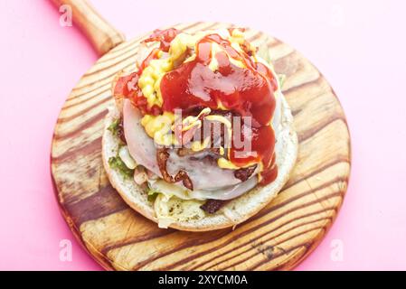 Hamburger, mit geschmolzenem Käse, Zwiebeln, Paprika, Speck, Ketchup, Senf, scharfer gemahlener Pfeffer, asturisches Rindfleisch, Spanien. Rosafarbener Hintergrund Stockfoto