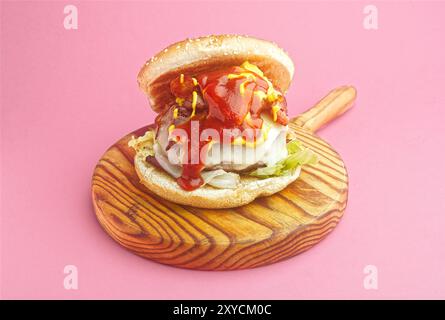 Hamburger, mit geschmolzenem Käse, Zwiebeln, Paprika, Speck, Ketchup, Senf, scharfer gemahlener Pfeffer, asturisches Rindfleisch, Spanien. Rosafarbener Hintergrund Stockfoto