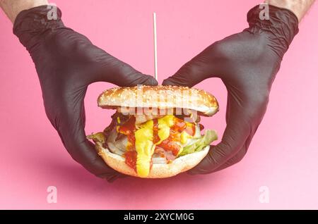 Hamburger, mit geschmolzenem Käse, Zwiebeln, Paprika, Speck, Ketchup, Senf, scharfer gemahlener Pfeffer, asturisches Rindfleisch, Spanien. Rosafarbener Hintergrund Stockfoto