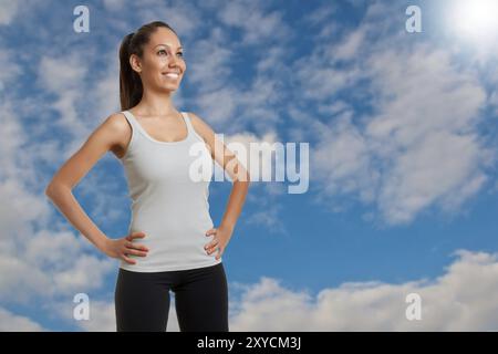 Sportliche Frau, die Arme ruhen auf ihre Taille mit einem wolkigen Himmel hinter ihr stehend Stockfoto