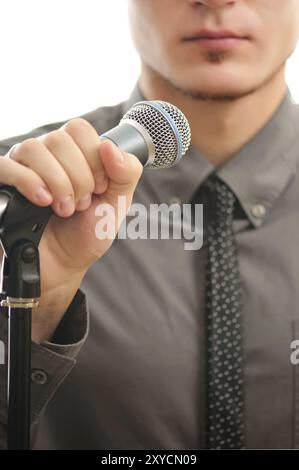 Geschäftsmann oder Sänger im grauen Mantel mit Krawatte, die das Mikrofon in der Hand hält, mit flachem Faden und Fokus auf das Mikrofon Stockfoto