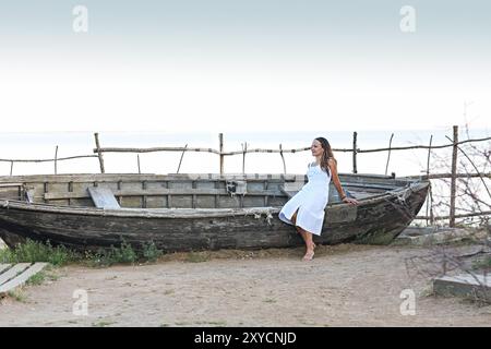 Junge Frau in weißem Kleid sitzt auf dem alten Boot durch das Meer. Altmodische Stockfoto