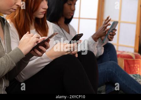 Drei junge Frauen benutzen Smartphones, während sie auf einem Sofa sitzen Stockfoto