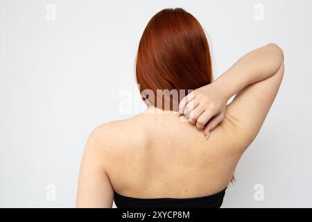 Die junge Frau kratzt sich mit der Hand auf weißem Hintergrund auf den Rücken Stockfoto