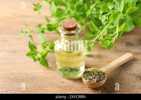 Ätherisches Öl in der Flasche, Löffel mit trockenem Kraut und Oregano-Zweigen auf Holztisch, Nahaufnahme Stockfoto